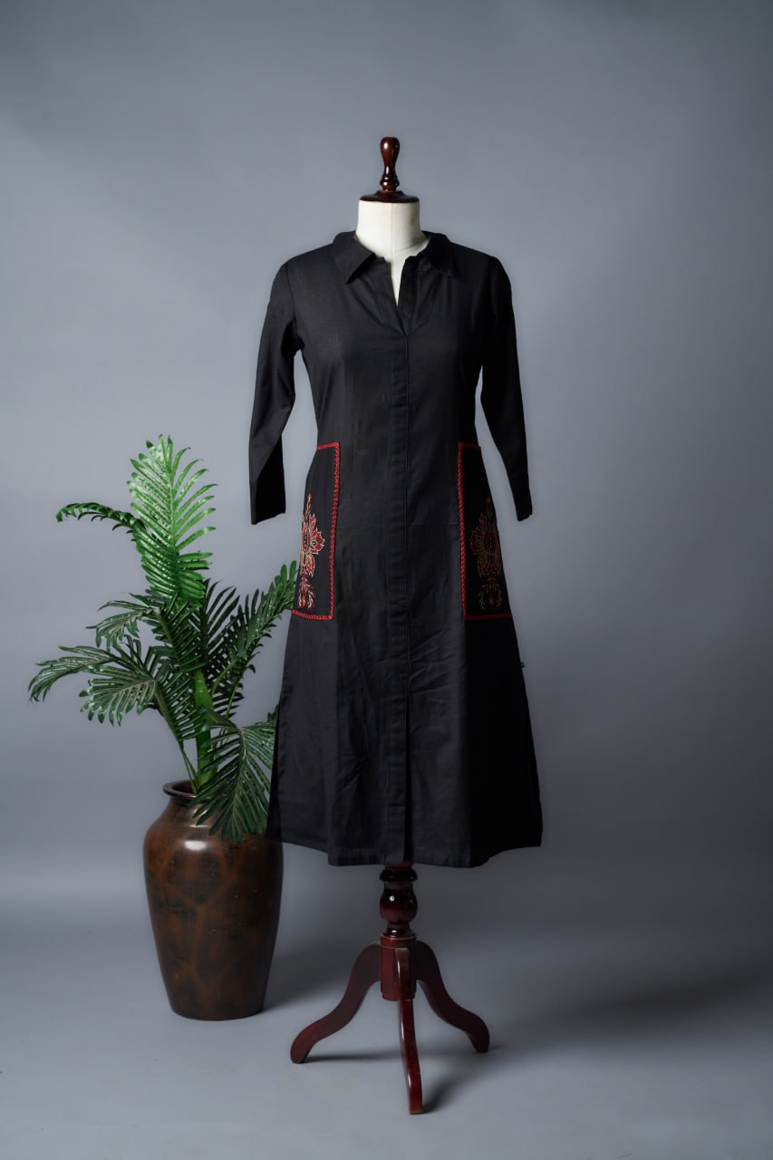 Black dress with red accents on a mannequin next to a plant and vase against a grey background