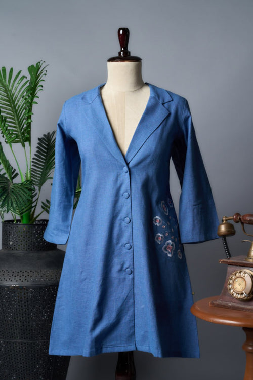 Blue coat on a mannequin against a gray background with a plant and vintage phone.